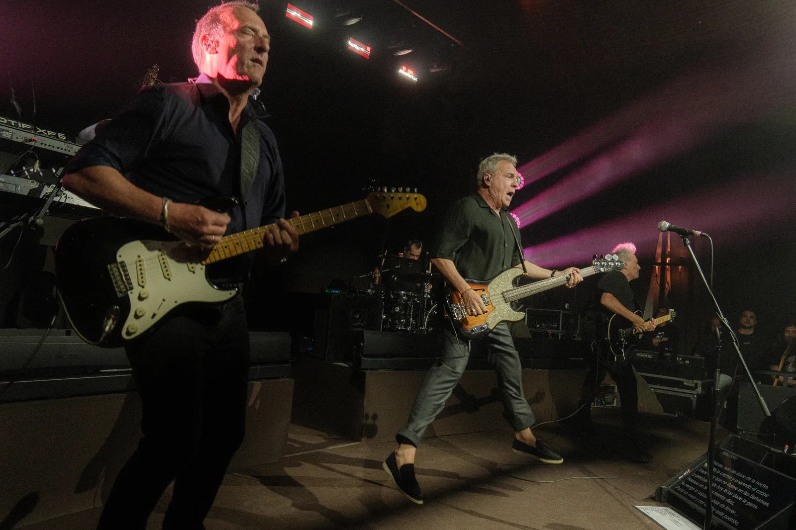 Guitarist and bass player performing on stage, wide-angle framing with the crowd in the background