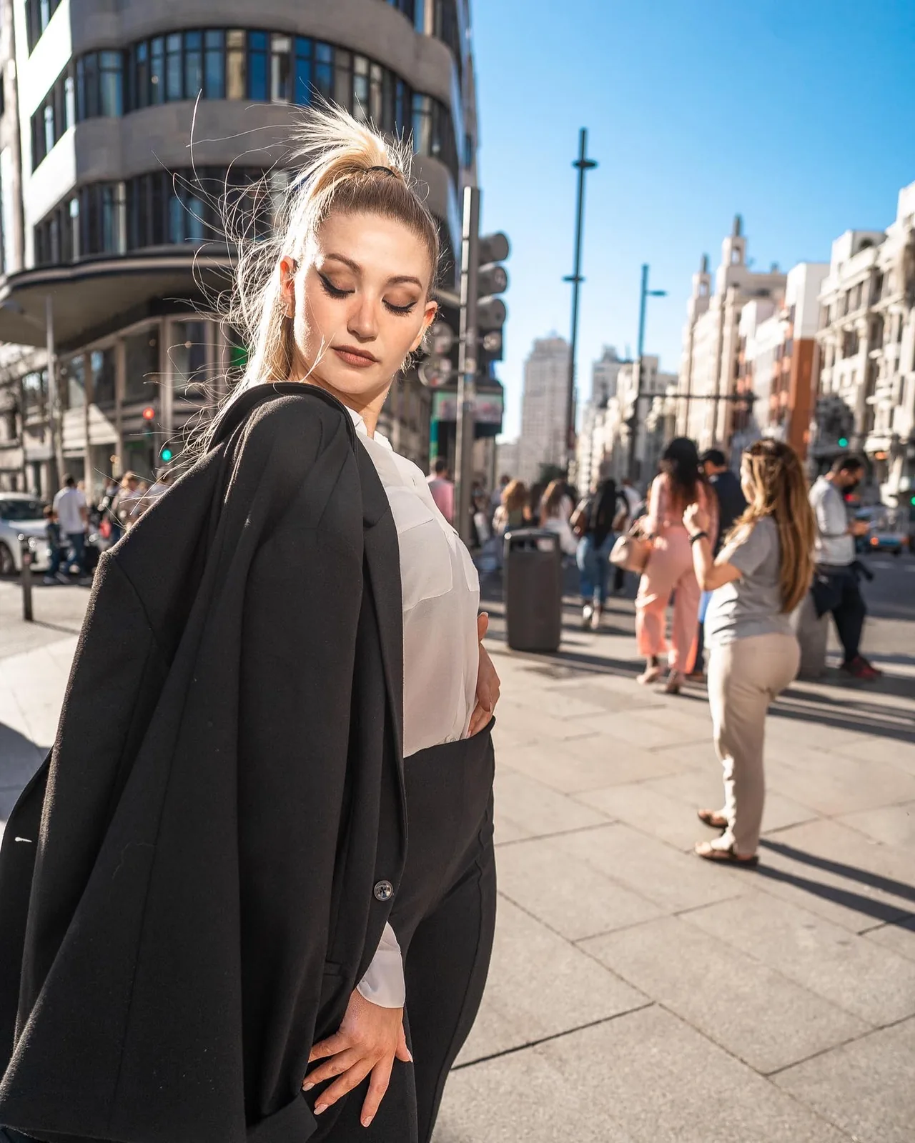 Modelo mirando por encima del hombro con un blazer negro sobre los hombros y la Gran Vía de Madrid al fondo