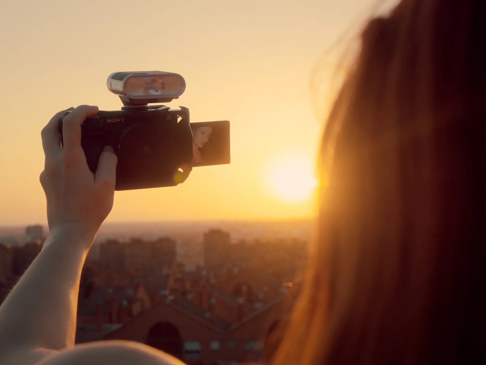 The sun as a small, low disc on Madrid's horizon, backlit next to a camera during golden hour